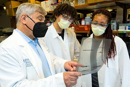 1 man gray hair, 2 students, all 3 in lab coats with masks