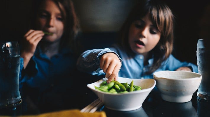 two little girls eating a bowl of edamame