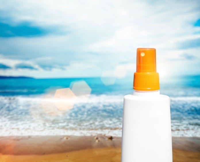 a bottle of sunscreen sits on a sandy beach with ocean in background