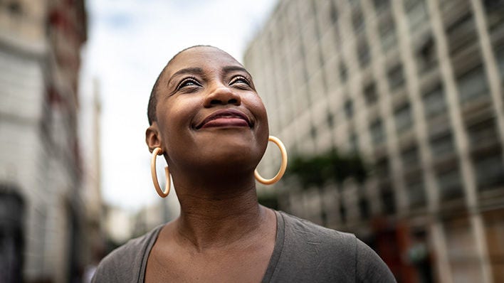 black woman with short hair looking up at sky scrapper buildings 