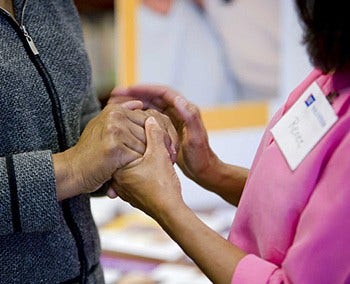 An ACS volunteer is comforting another person by holding both their hands.