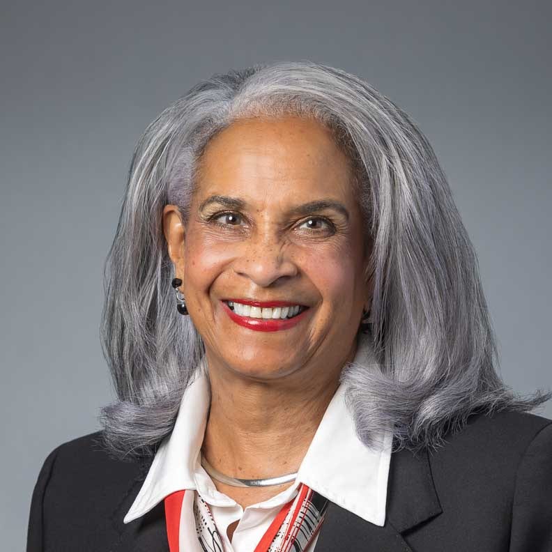 Smiling woman with gray hair wearing blazer against neutral background.
