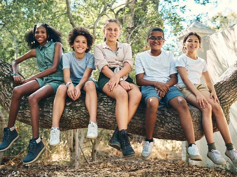 Five kids sit on a large tree limb