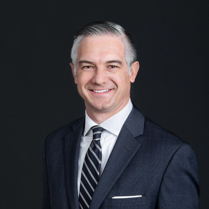 Man in dark suit with striped tie, smiling professionally