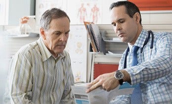 Photo of a male doctor with a senior male patient going over a brochure in medical office.