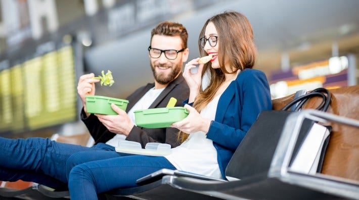 couple sitting in waiting area of airport eating fruit and vegetables