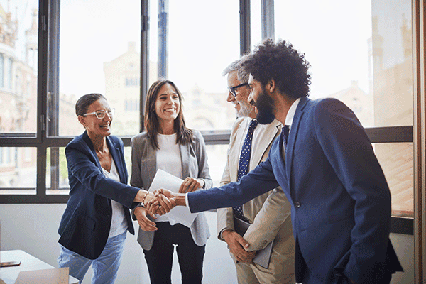 Business professionals smiling and shaking hands in office meeting.