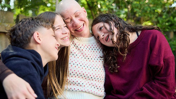 Padre sonriendo con tres hijos al aire libre.