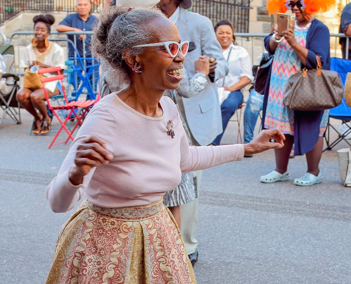 black elderly woman wearing skirt and sunglasses walking down street