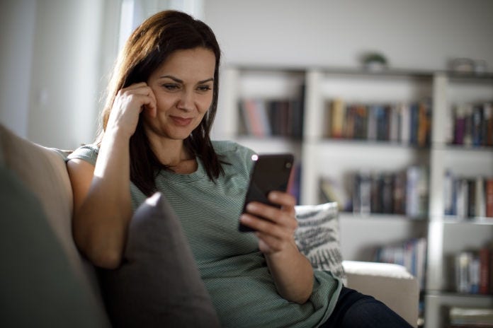 white woman looking at cell phone while sitting on couch