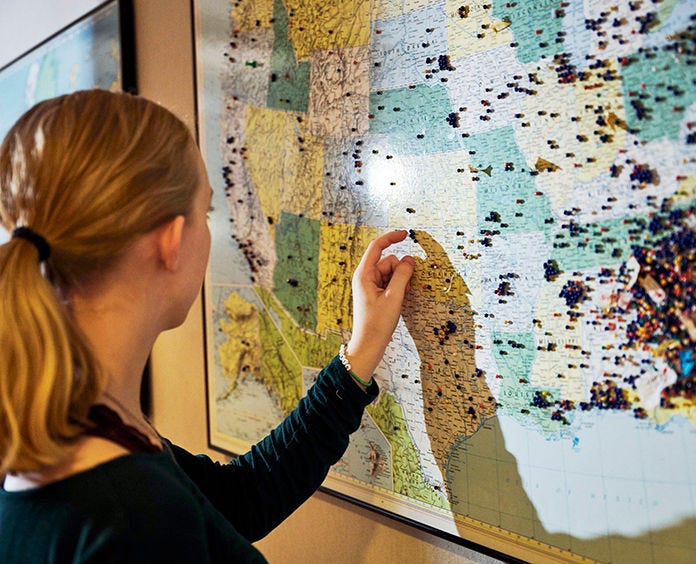 white woman with ponytail touching US map with push pins
