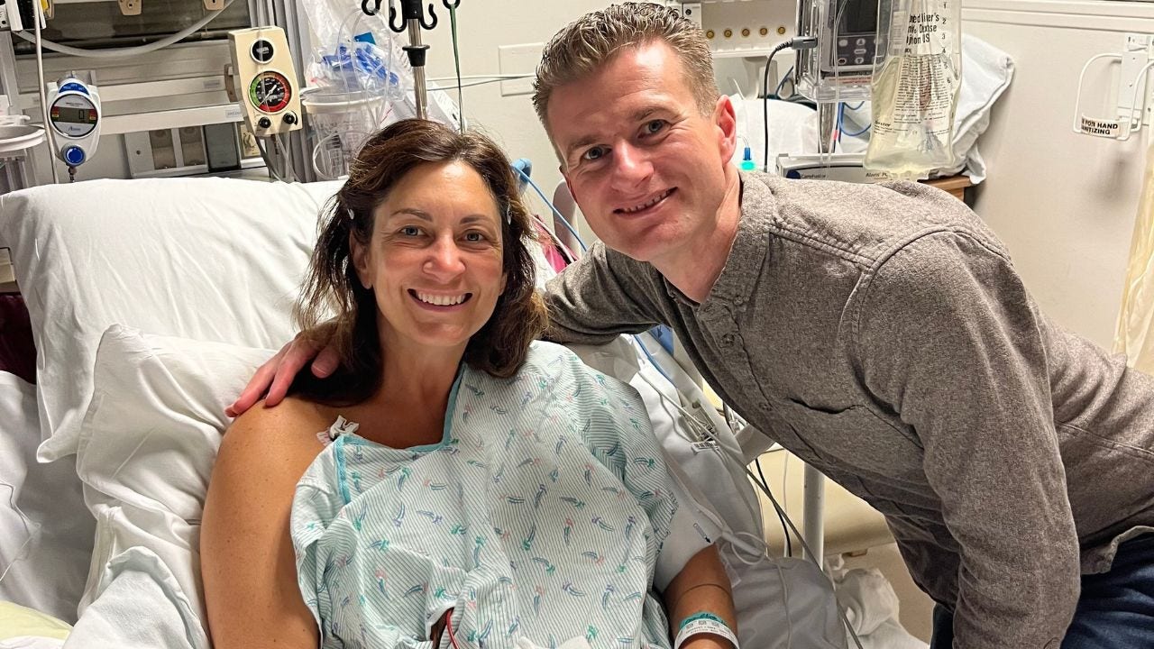 Dr. Emily Williams and a supporter smile for a photo while she sits in a hospital bed 