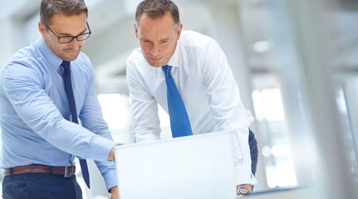 two men stand and work in front of office computer