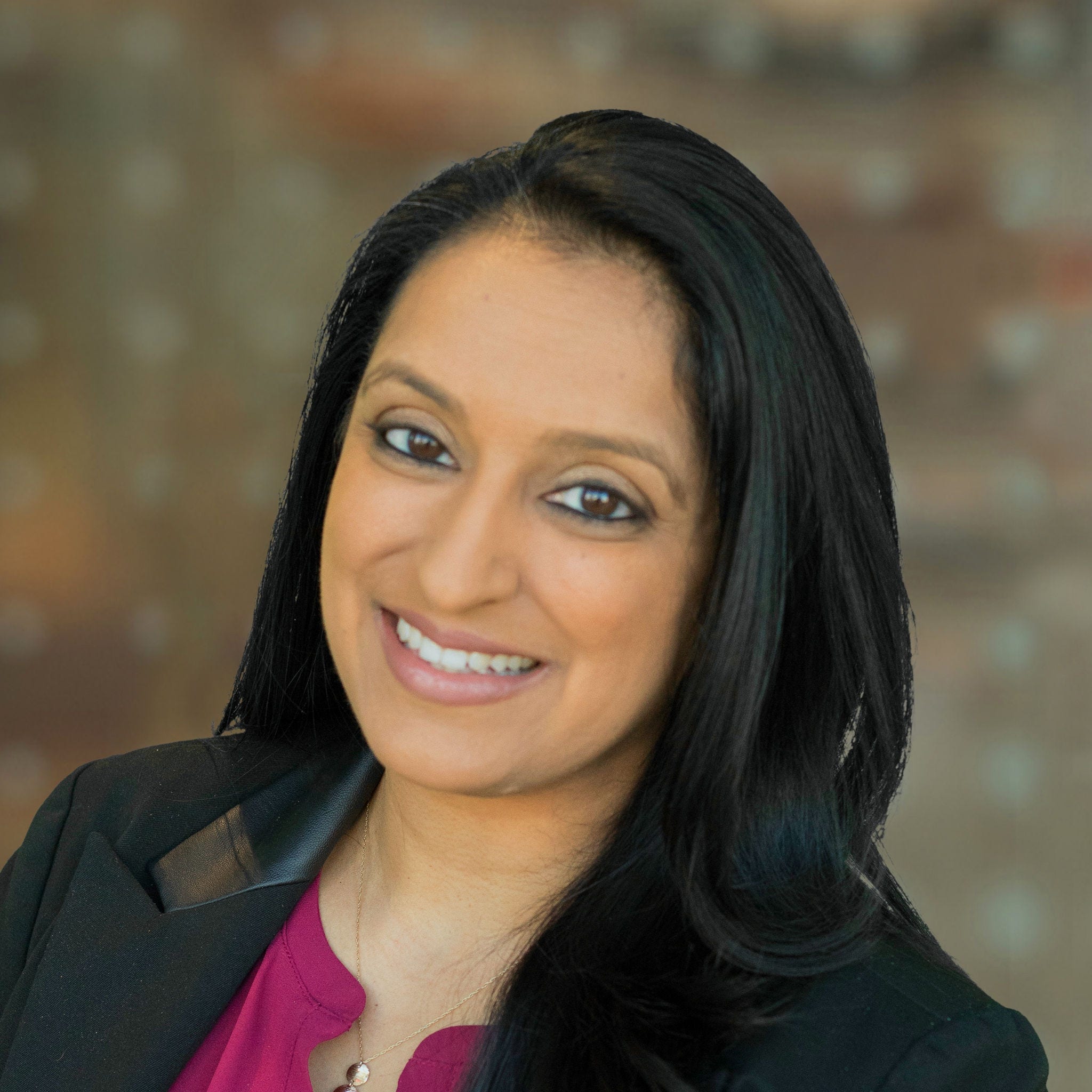 Woman, med brown skin tone, long black hair, black blazer, maroon blouse, 3-circle necklace