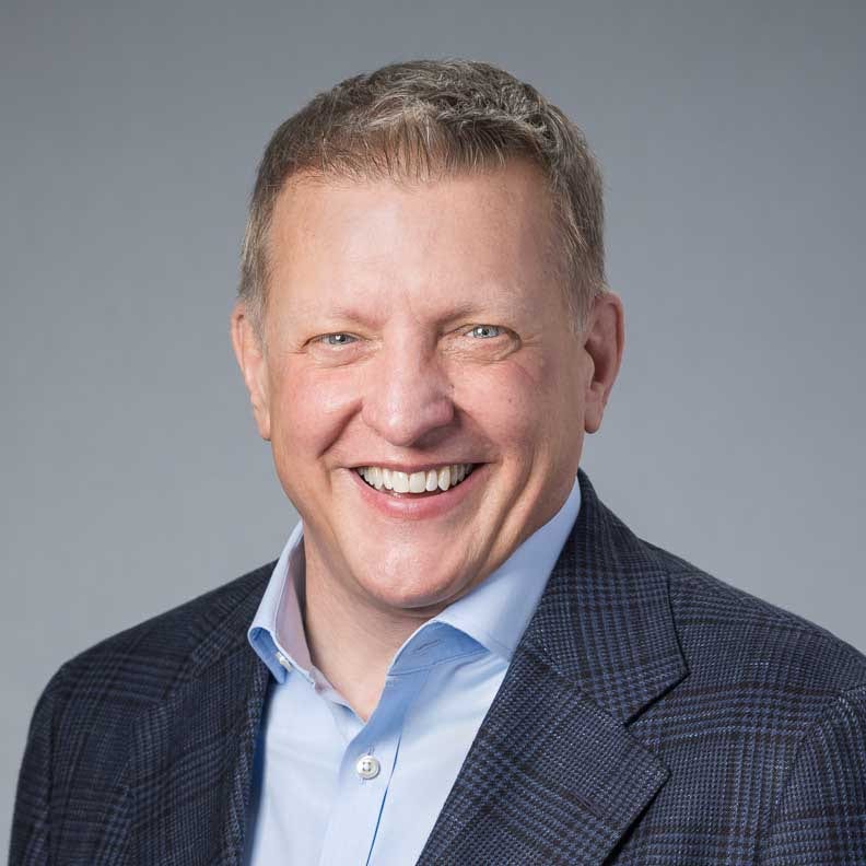 Smiling man in blue dress shirt and plaid blazer.