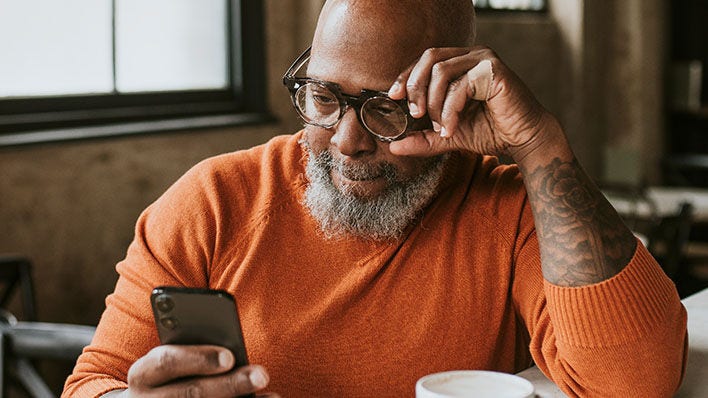 Hombre mayor con gafas mirando un teléfono inteligente en interiores.