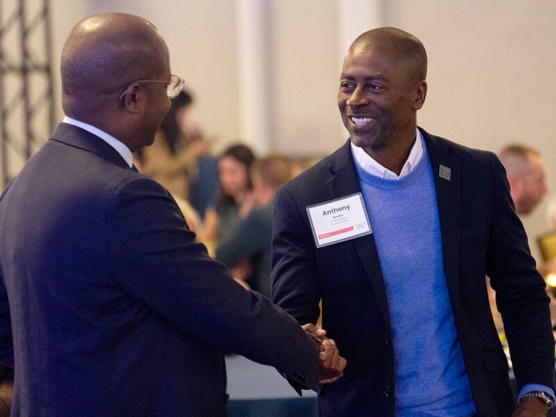 Two men shaking hands at networking event, smiling.