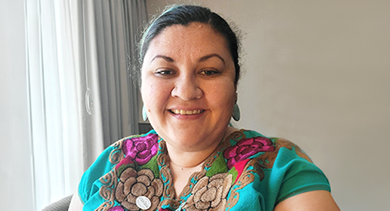 Mujer sonriente con blusa turquesa bordada en interiores.