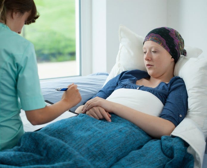 teen girl in head scarf lies in hospital bed and talks to nurse