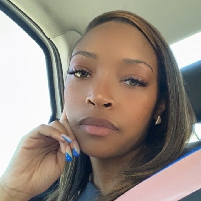 Black woman in car with hand on face blue fingernails