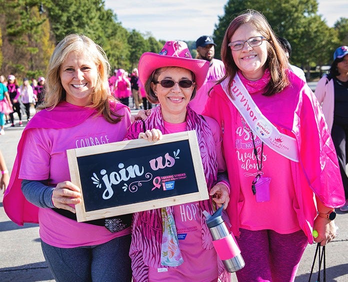 three women wearing pink holding a join us sign for volunteer opportunities