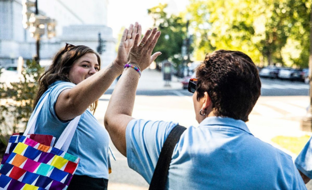 Two women in blue shirts share a celebratory high five.