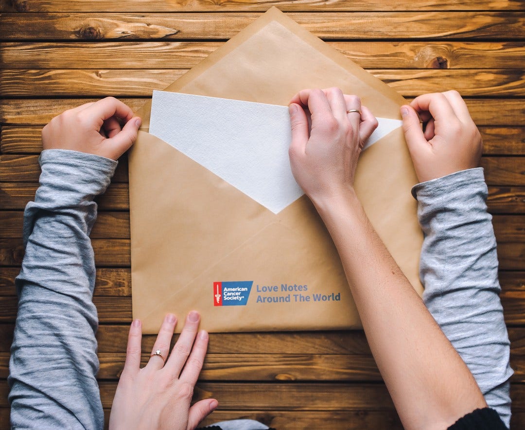 two people's hands holding large envelope with ACS Love Notes logo printed on it