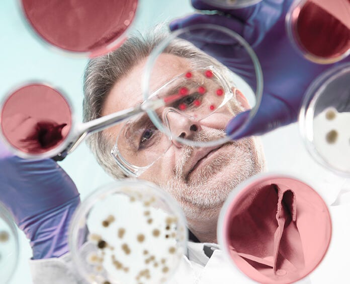 Scientist seen through several Pertri dishes with a pipette