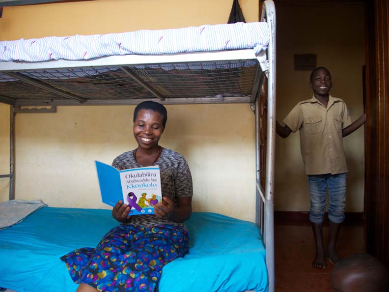 Two African American children in a room with bunk beds one sitting on bottom bunk reading a book the other standing by the door