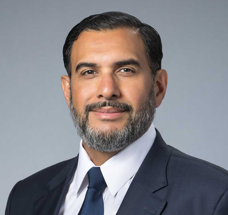 Professional man with beard wearing suit and tie, neutral background.