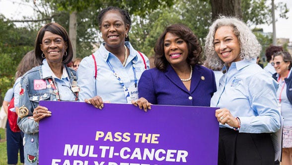 Four women stand outside with a banner for an event.