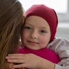 A child wearing a maroon head covering hugs a person with long brown hair.
