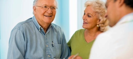 smiling senior couple talk with doctor in office