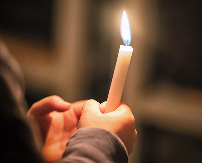 white person holding a single candle in the dark