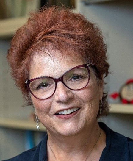 Headshot of research professor Electra Paskett, PhD, MSPH, in a navy top and maroon eyeglasses.