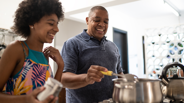 Black father and daughter smiling while cooking a meal on the stove