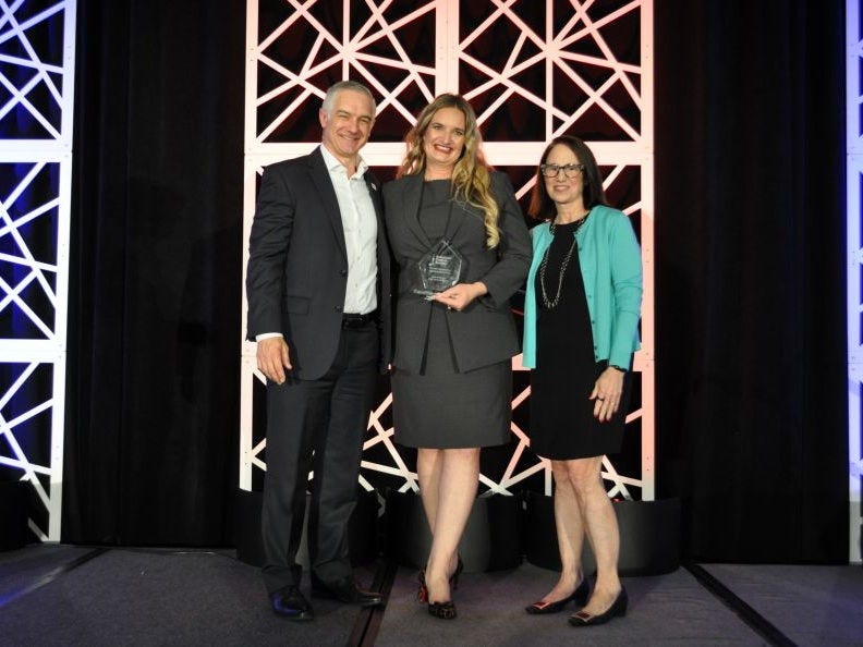 Three people posing on stage with an award.