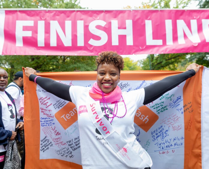 Black female survivor holding team flag at finish line of event