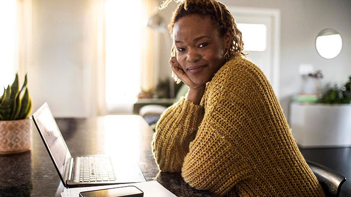 Smiling woman sitting at a table with a laptop and phone.