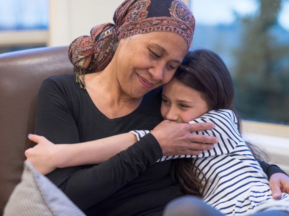 Image of a young girl hugging an older woman who is wearing a scarf on hear head