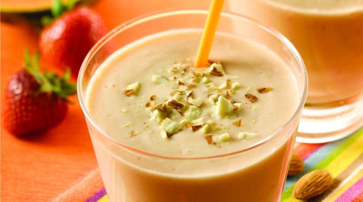 glass of papaya and almond smoothie sitting on table with almonds and strawberries in background