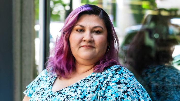 Una mujer con el cabello teñido de púrpura posando con confianza al aire libre.