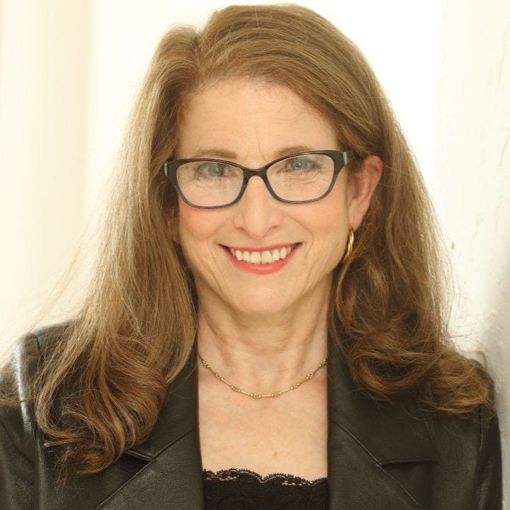 woman with long red hair and dark glasses wearing dark gray jacket and lacey black shirt