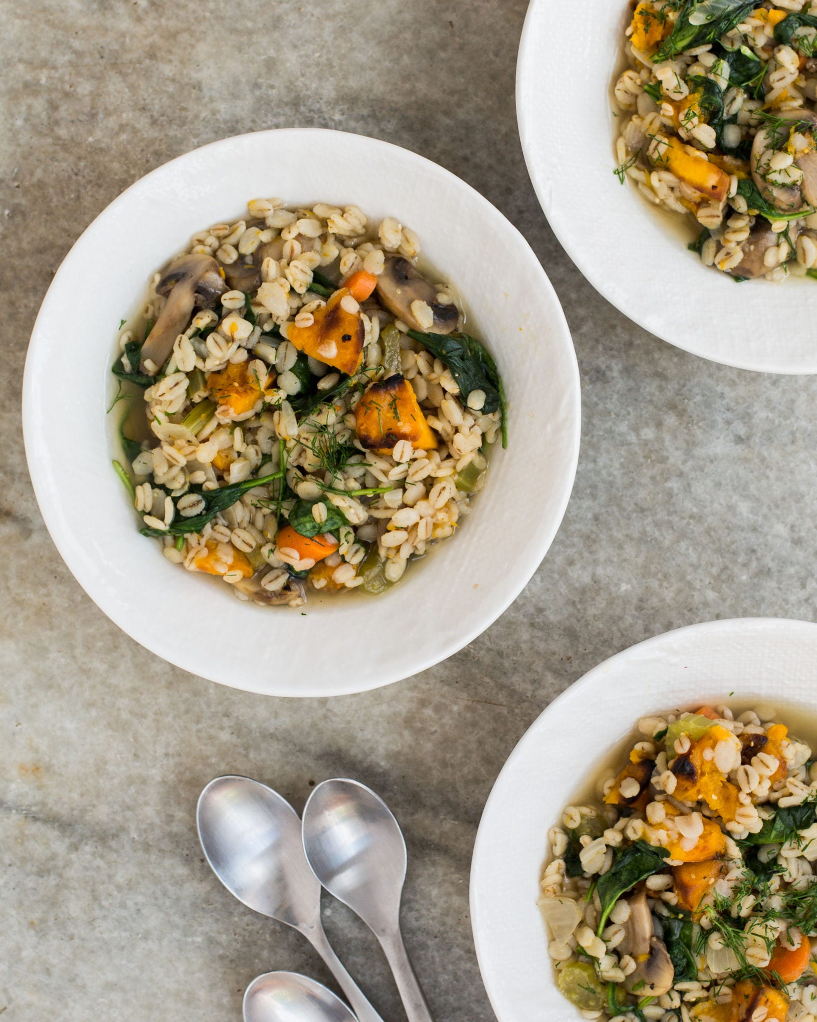 Three white bowls filled with butternut squash and barley stew sit on a marble countertop.