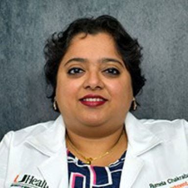 woman with short curly dark hair white jacket with black shirt with pink and white squares