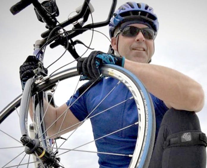 man in blue shirt and helmet holding up a bike