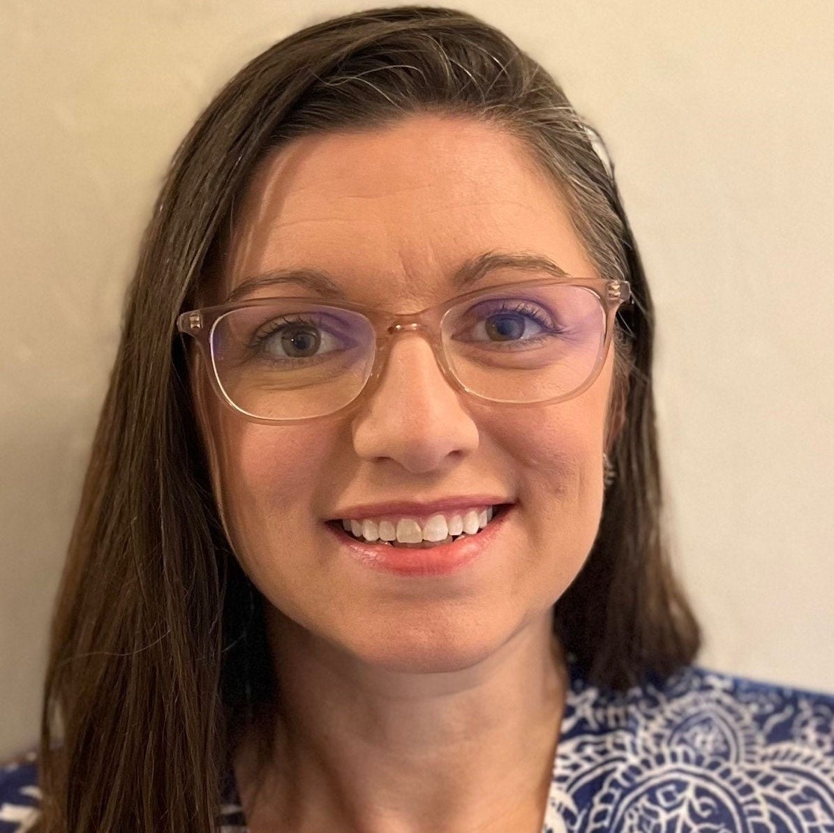 White woman, long brown hair, clear glasses, blue and white patterned blouse