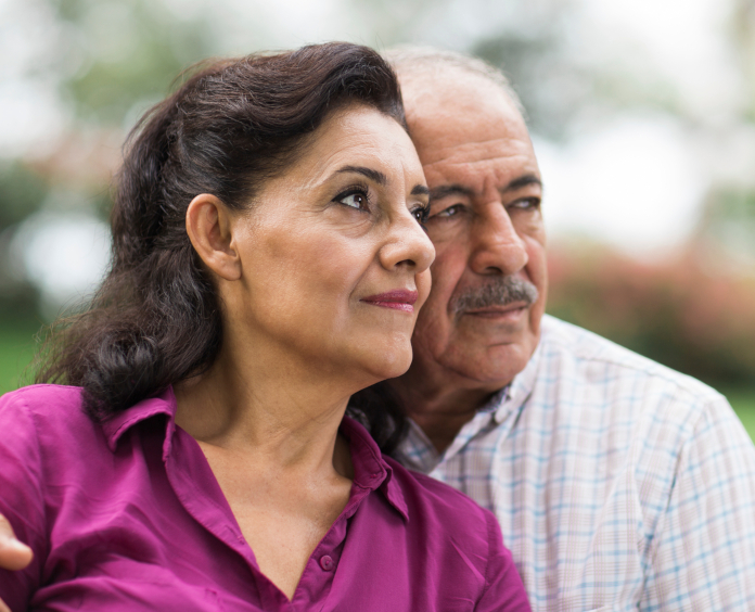 A serious senior Hispanic couple looking away in a horizontal head and shoulders shot outdoors.