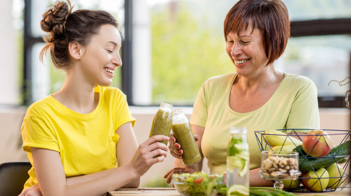 mom and daughter have smoothies at kitchen table