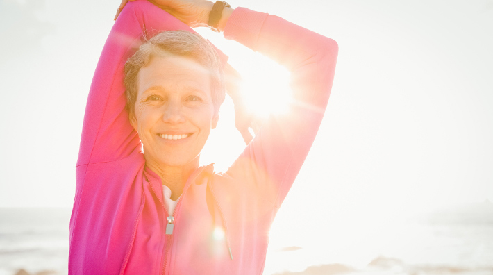 smiling middle aged woman stretches on sunny beach before exercise